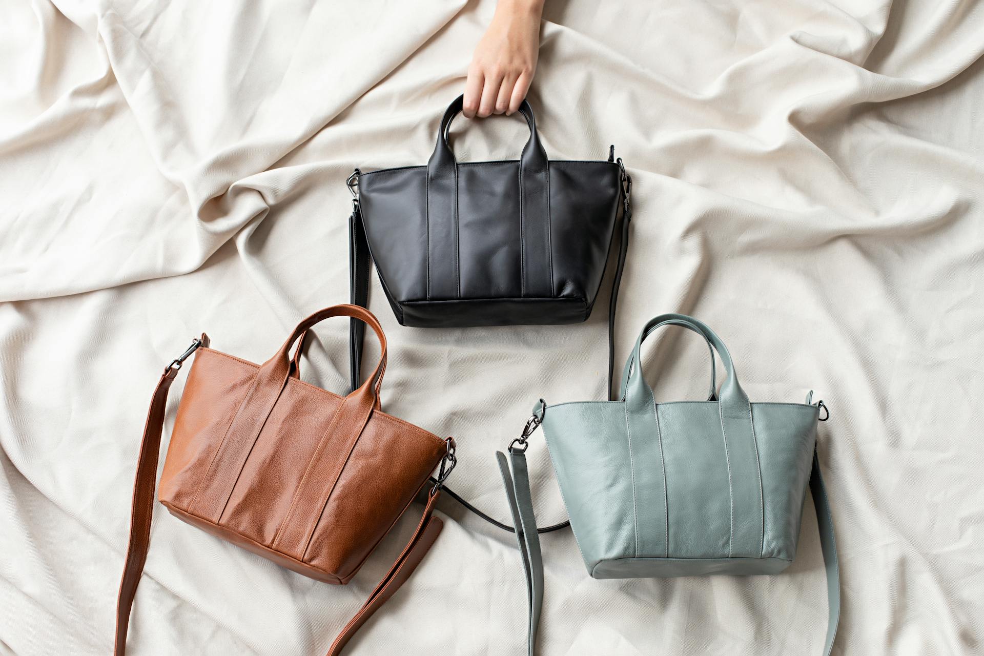 Three handbags in black, brown, and green on a light fabric background